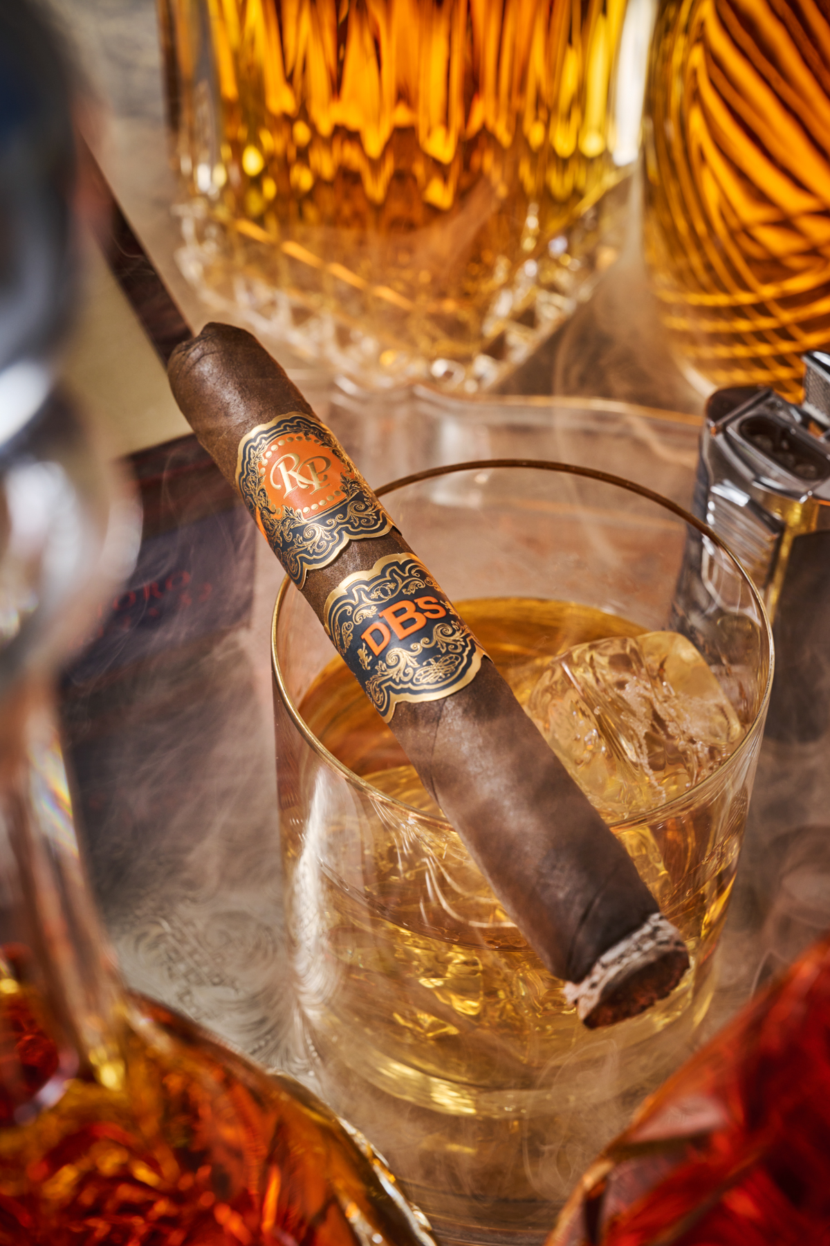 A single cigar resting on a tumbler of whisky in low evening light, smoke drifting.